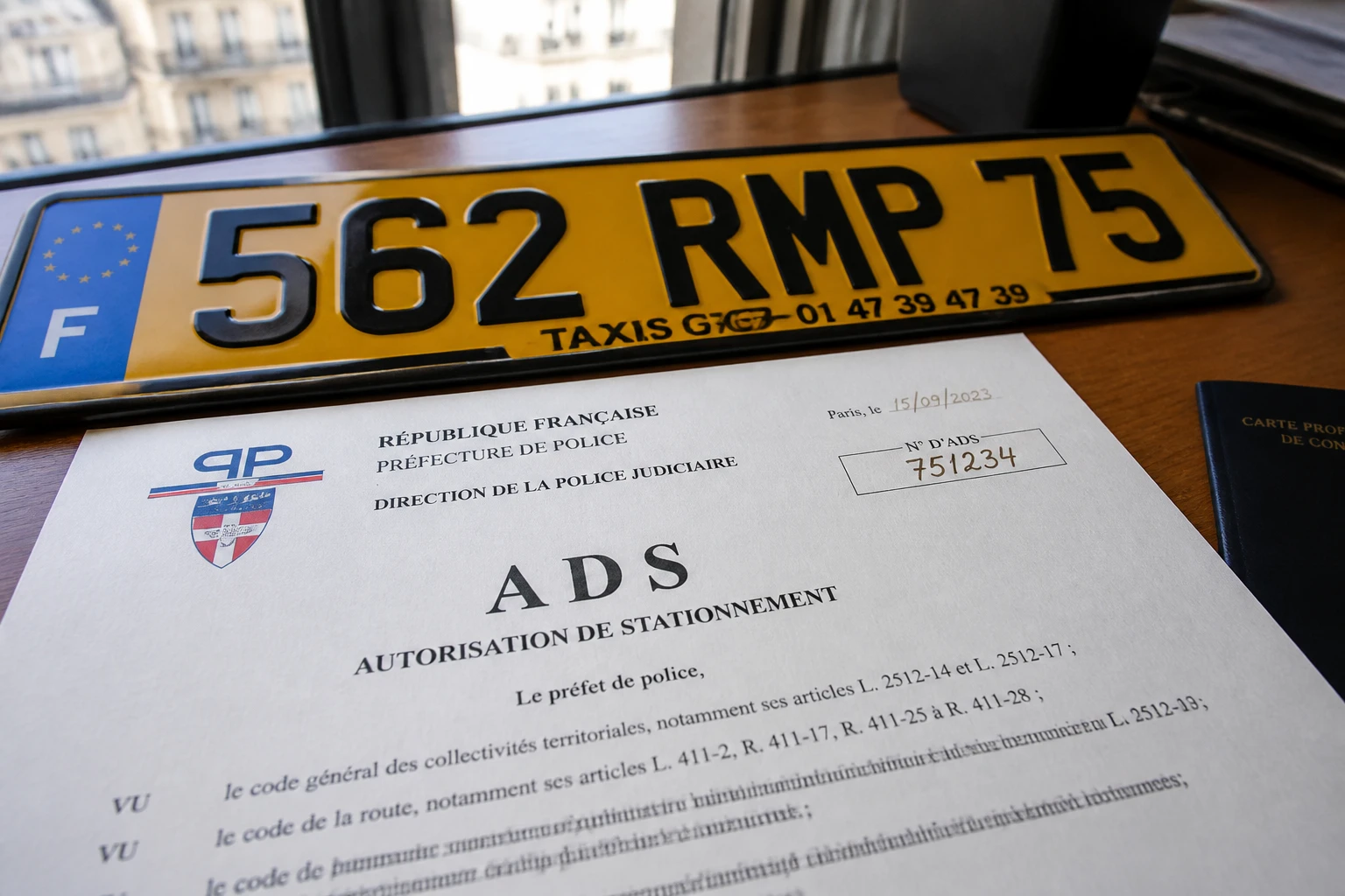 Document officiel d'autorisation de stationnement ADS et plaque de taxi posés sur un bureau à Paris