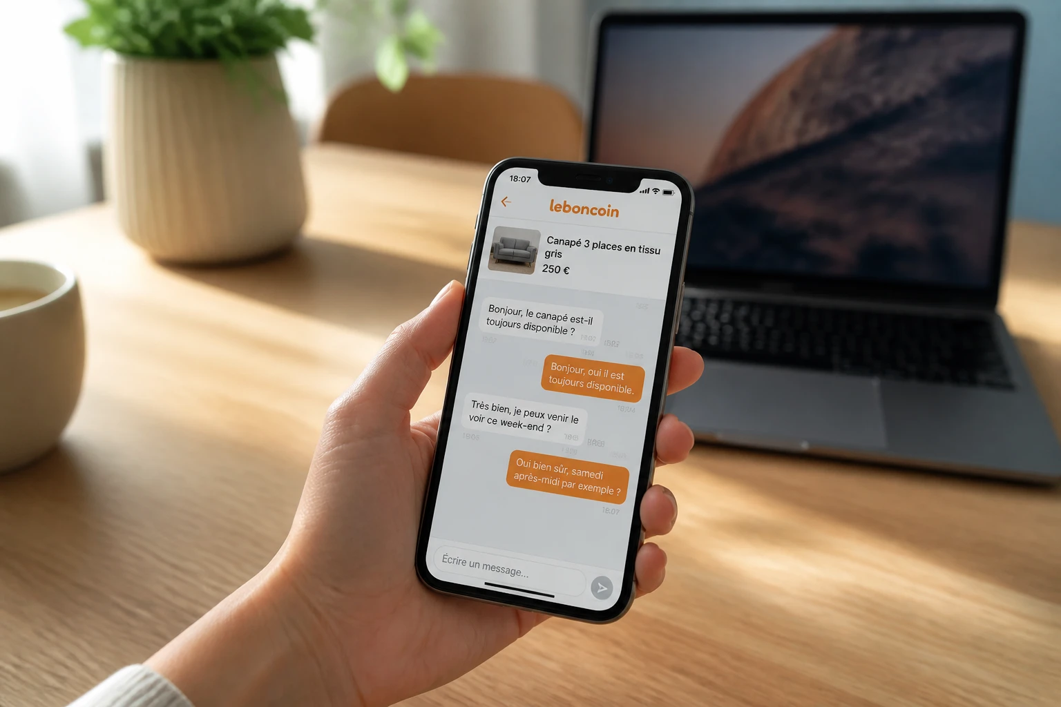 Smartphone affichant une messagerie Leboncoin sur un bureau, ordinateur portable en arrière-plan