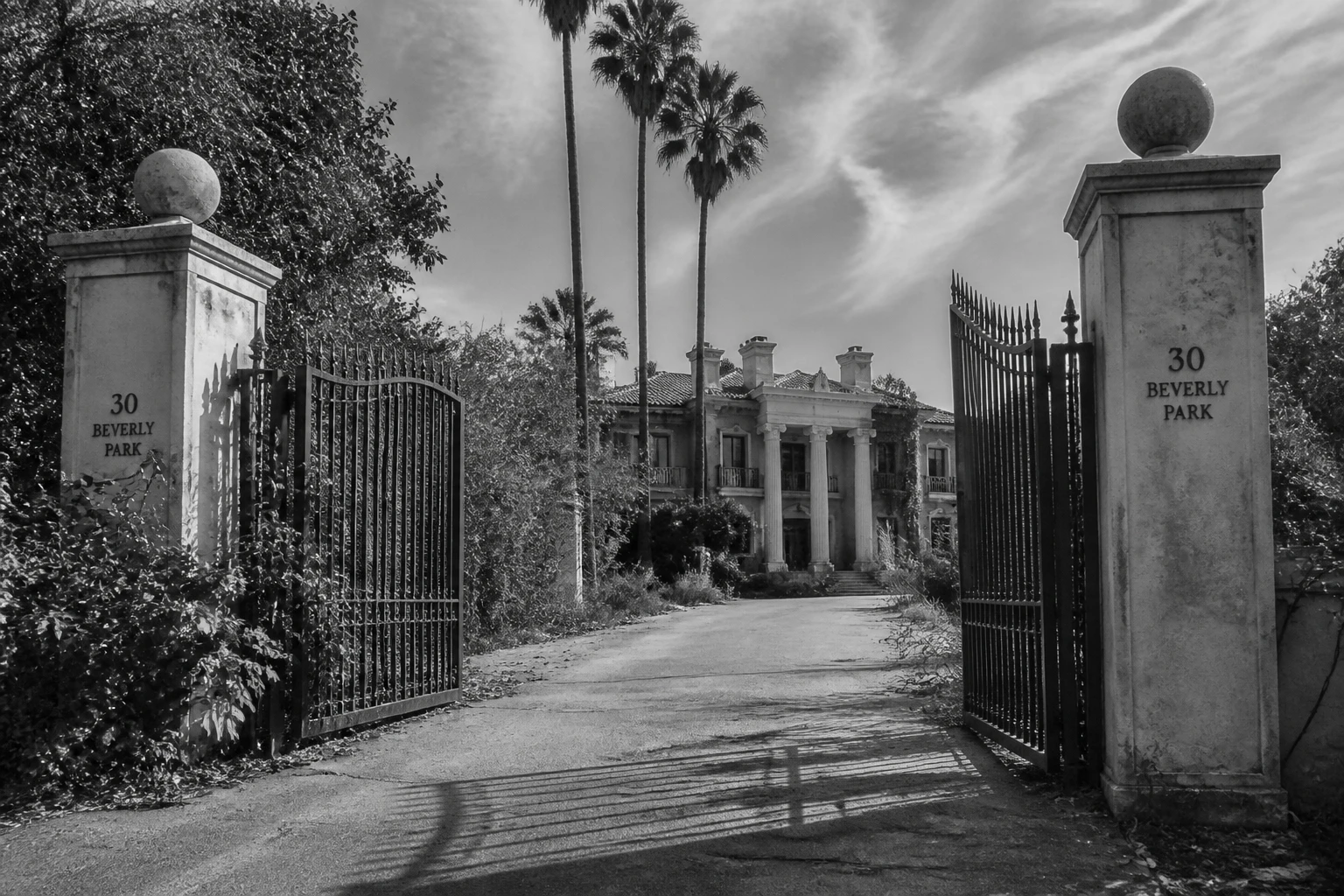 Entrée d'une villa de luxe abandonnée à Beverly Hills, grilles en fer forgé et haies envahissantes